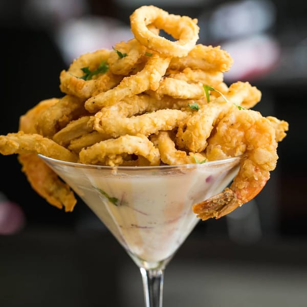 Crispy fried calamari and shrimp in a martini glass with creamy sauce, a Peruvian Cebiche-Bar dish.