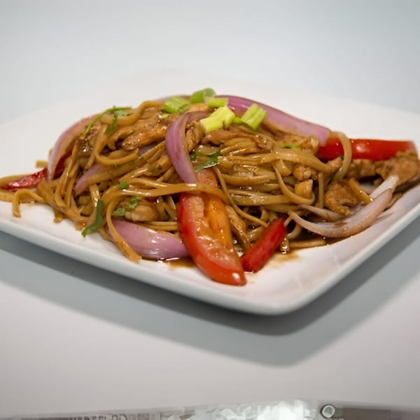 Peruvian Lomo Saltado with noodles, red onions, tomatoes, and green onions on a white plate.