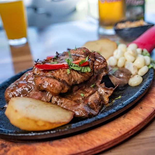 Peruvian grilled meat with potatoes, corn, and red peppers on a sizzling platter.