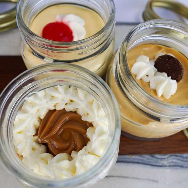 Three Peruvian desserts in glass jars, topped with whipped cream, dulce de leche, and a cherry.
