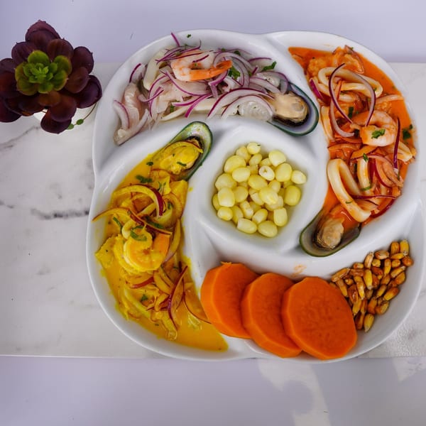 Peruvian ceviche sampler with seafood, red onions, corn, and sweet potato on a white platter.