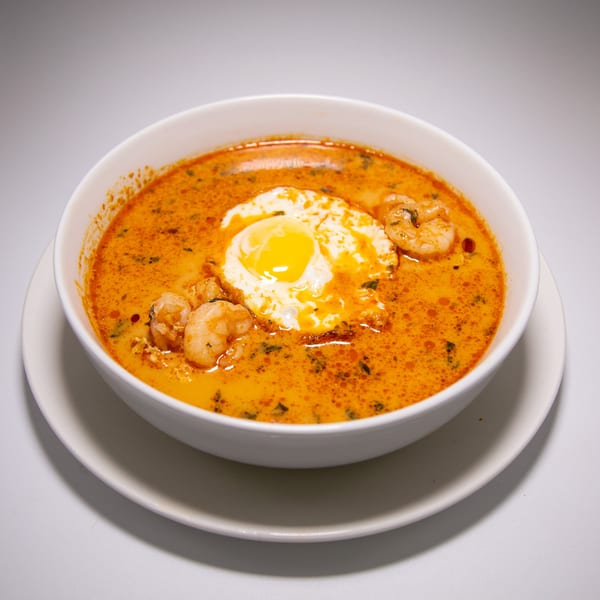 Peruvian shrimp soup with a fried egg and herbs in a white bowl.
