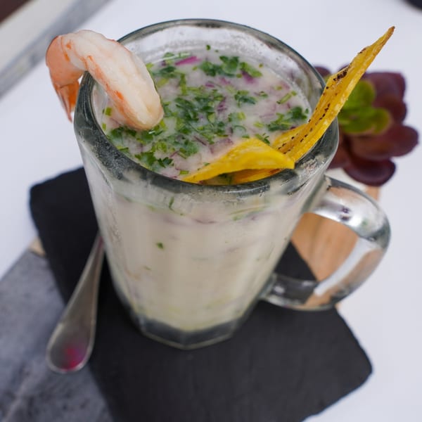Peruvian leche de tigre cocktail with shrimp, plantain chip, cilantro, and red onion in a glass mug.