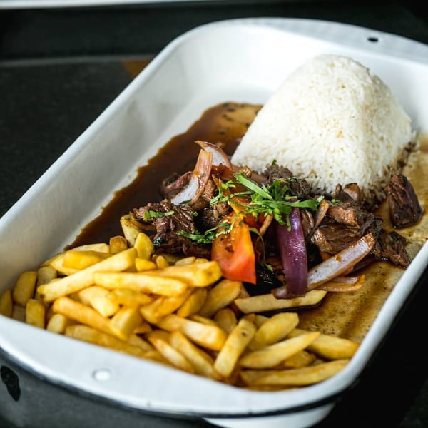 Peruvian Lomo Saltado with beef, onions, tomatoes, fries, and rice in a white dish.