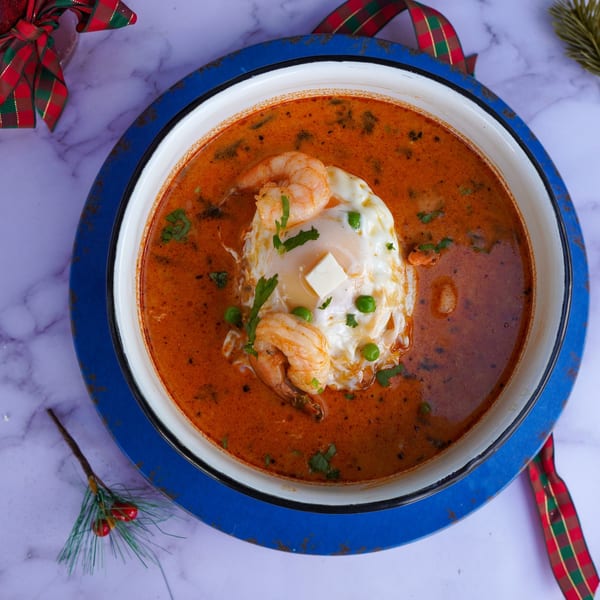 Peruvian Parihuela soup with shrimp, a poached egg, peas, and cilantro in a blue bowl.