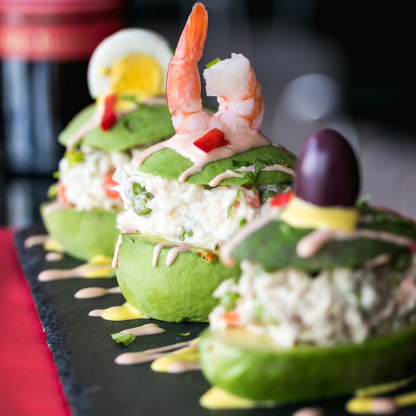 Peruvian avocado rellenos, one topped with shrimp, another with a hard-boiled egg, and a third with an olive.