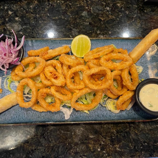 Crispy fried calamari rings on lettuce with red onion, lime, and dipping sauce on a blue plate.