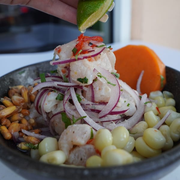 Hand squeezing lime over a Peruvian ceviche with shrimp, red onion, corn, and sweet potato.